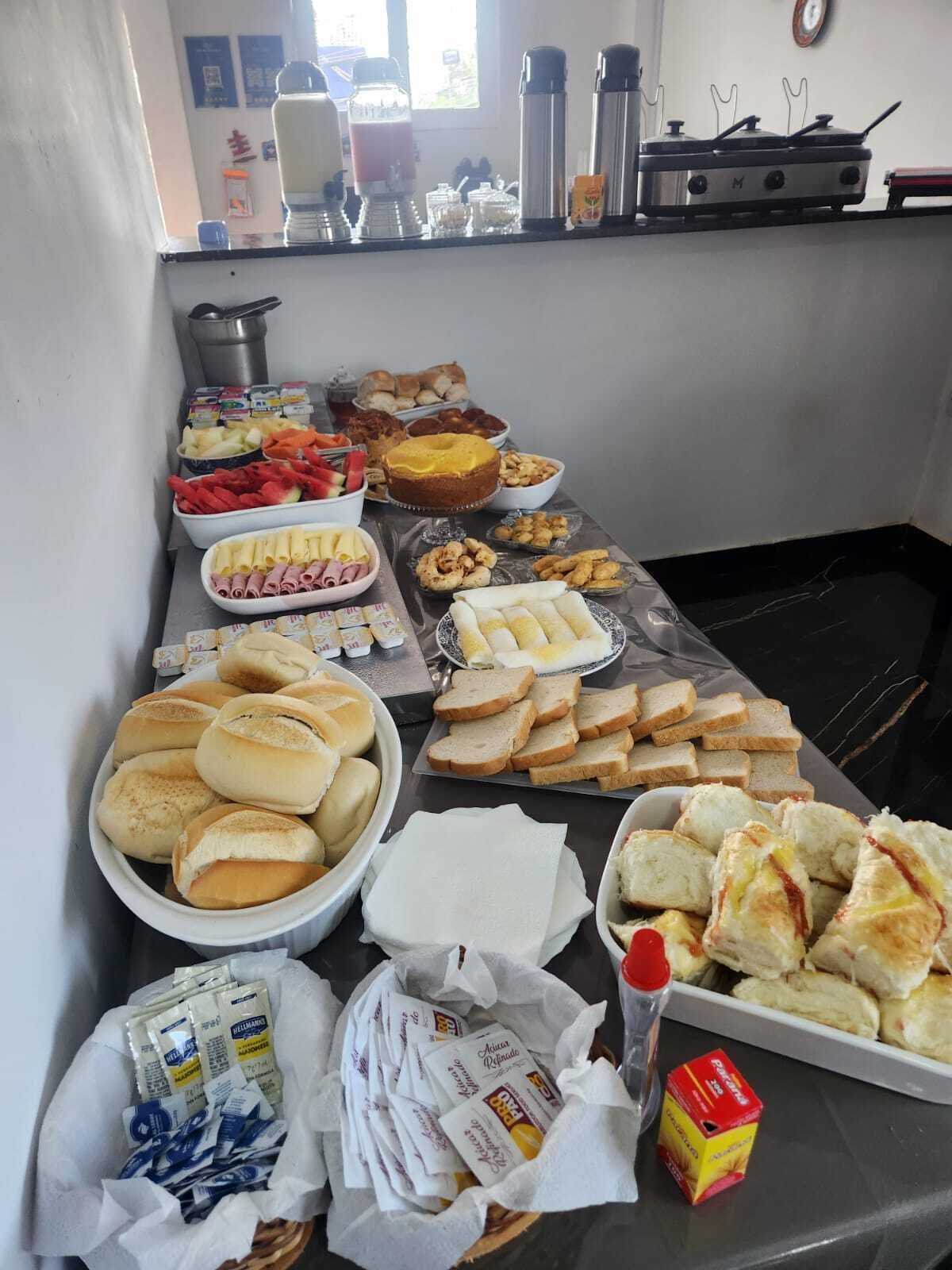 Une table de buffet proposant divers aliments, notamment des petits pains, du pain, des pâtisseries et des condiments.