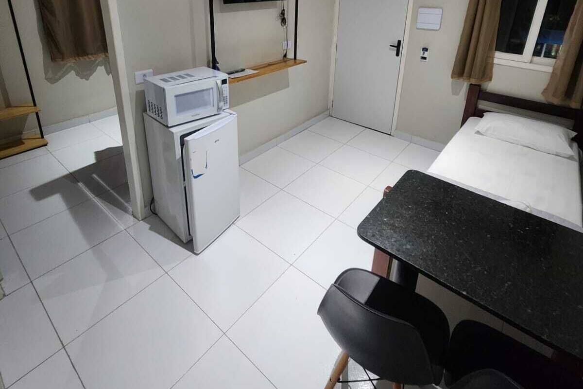 A compact kitchen with a microwave, a small refrigerator, a flat-screen TV mounted on the wall, and a dining area with a table and chairs.