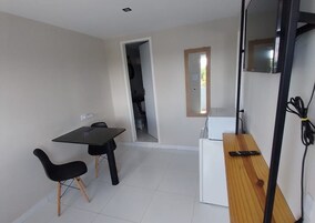 Una cocina pequeña y moderna con refrigerador, microondas y una mesa de madera. Se ve un ventanal con vistas a la vegetación.