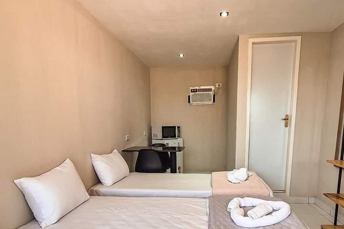 A hotel room with two beds, a desk with a computer, an air conditioner, and a door.