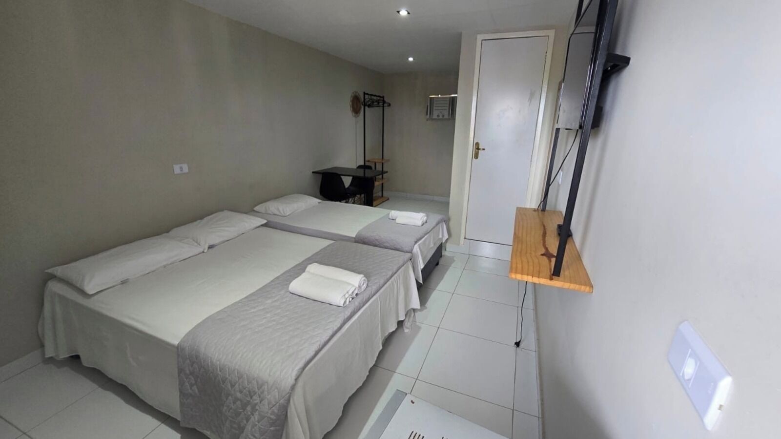 Habitación de hotel con dos camas individuales, una estantería de madera, un escritorio y un armario.