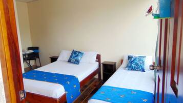 Una habitación con dos camas de madera, cada una con una colcha azul y almohadas blancas. Hay una mesita y una silla en la esquina.
