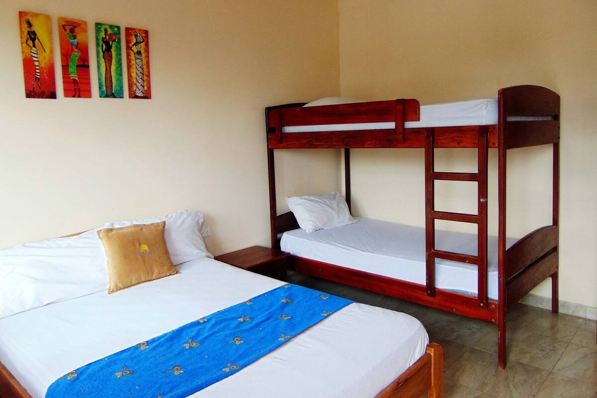 A room with a bunk bed, a single bed, and a nightstand. There are three paintings on the wall.