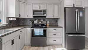 A modern kitchen with white cabinetry, a stainless steel refrigerator, a microwave, and an oven. - Blenheim Hideaway (Blenheim)