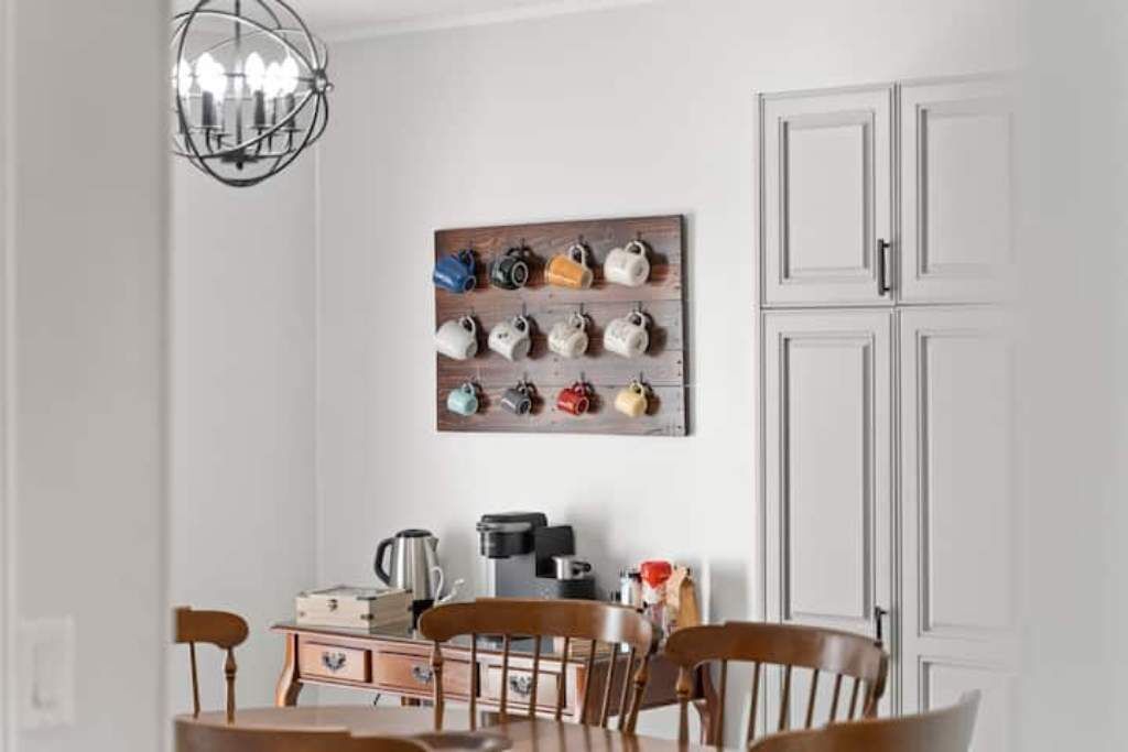 A dining area with a wooden table, chairs, a chandelier, and a wall-mounted mug rack.