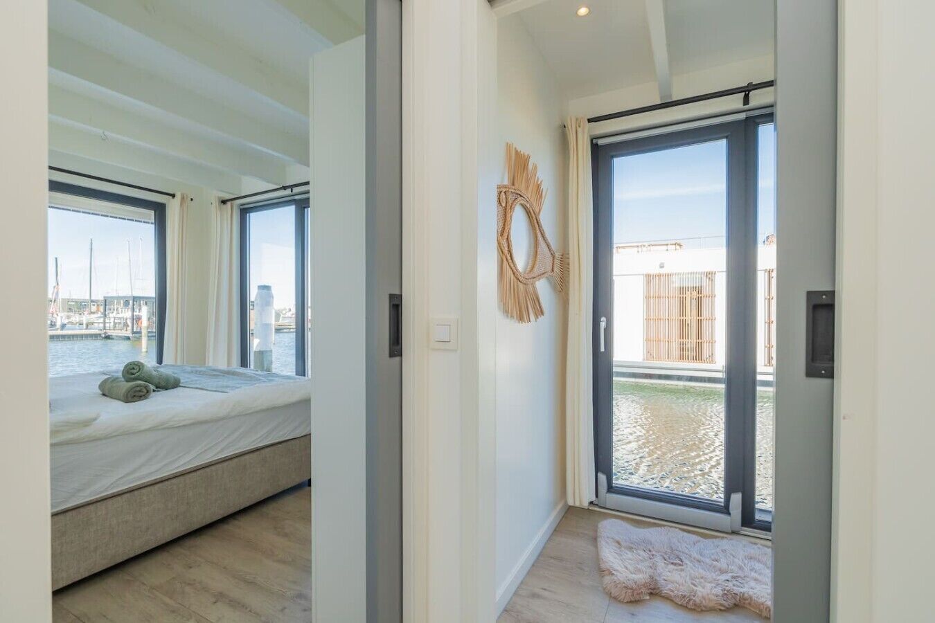 A modern room with a bed, a large window, and a view of a marina.