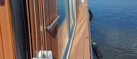 A view from a boat's window overlooking calm water, with a clear sky and distant land.