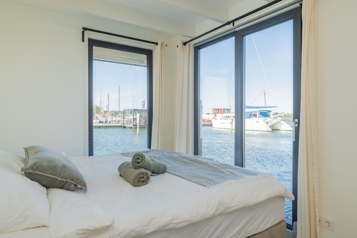 Une chambre avec un lit, deux fenêtres et une vue sur une marina remplie de bateaux.
