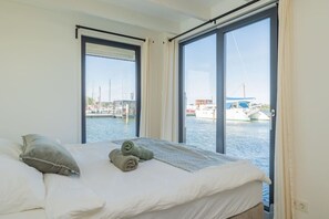 A room with a bed, two windows, and a view of a marina with boats. - Fantastic Houseboat `Splendid` with Tender Kaag (Monnickendam)