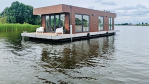 A modern floating house with a flat roof, large windows, and a deck with seating. - Fantastic Houseboat `Splendid` with Tender Kaag (Monnickendam)
