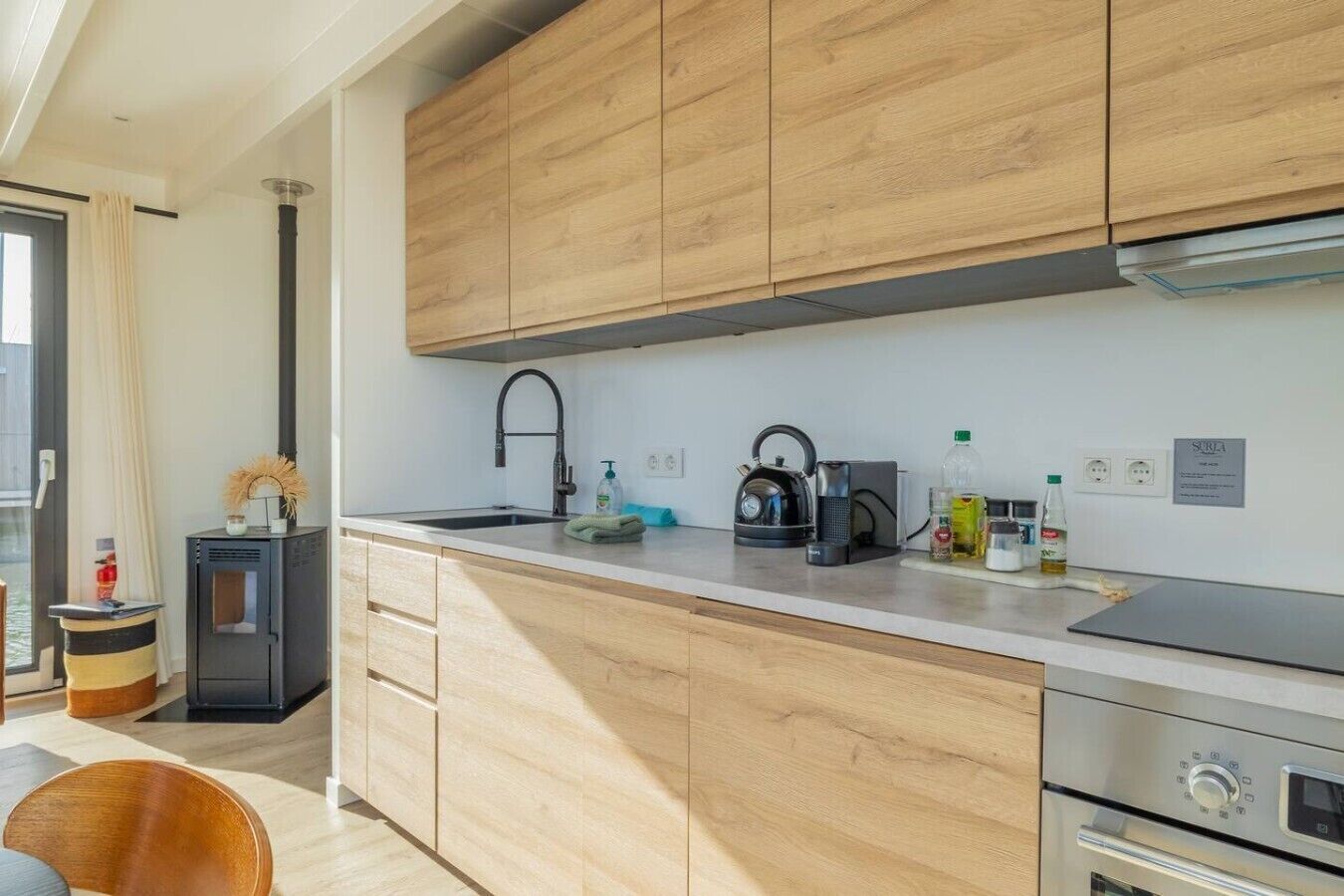 Una cocina moderna con armarios de madera, un lavamanos de acero inoxidable y un horno empotrado.