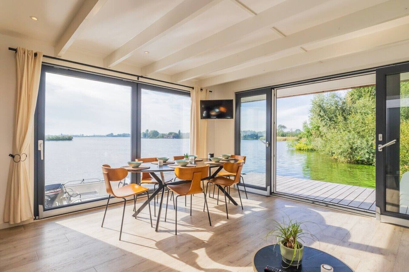 Un espace repas comprenant une table et des chaises, de grandes fenêtres et une vue sur une étendue d’eau.