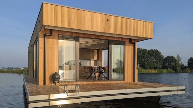 A floating wooden structure with a deck, glass doors, and a table with chairs.