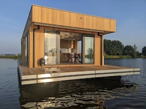 Una estructura de madera flotante con terraza, puertas de cristal y una mesa con sillas.