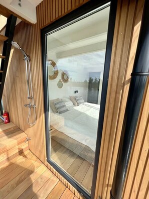 A modern bedroom with a large sliding glass door, a shower area, and a bed with pillows.