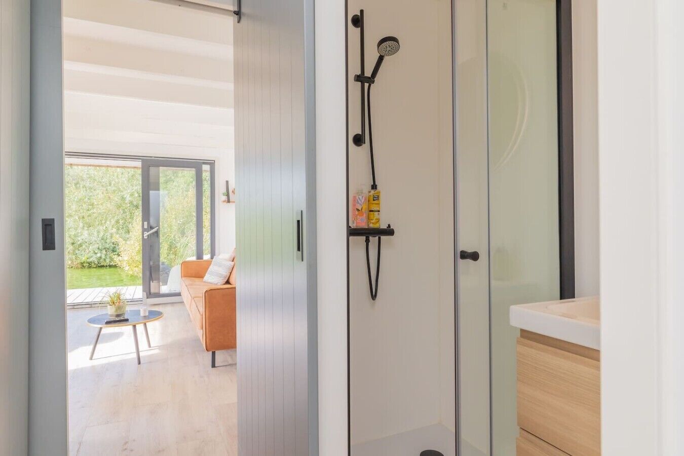 Een moderne badkamer met een glazen douchecabine, een handdoekrek met toiletartikelen en een uitzicht op een terras.