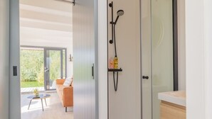 A modern bathroom with a glass shower enclosure, a towel rack with toiletries, and a view of an outdoor seating area.