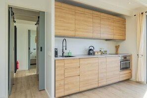 A modern kitchen with wooden cabinets, a built-in oven, and a kettle on the countertop.