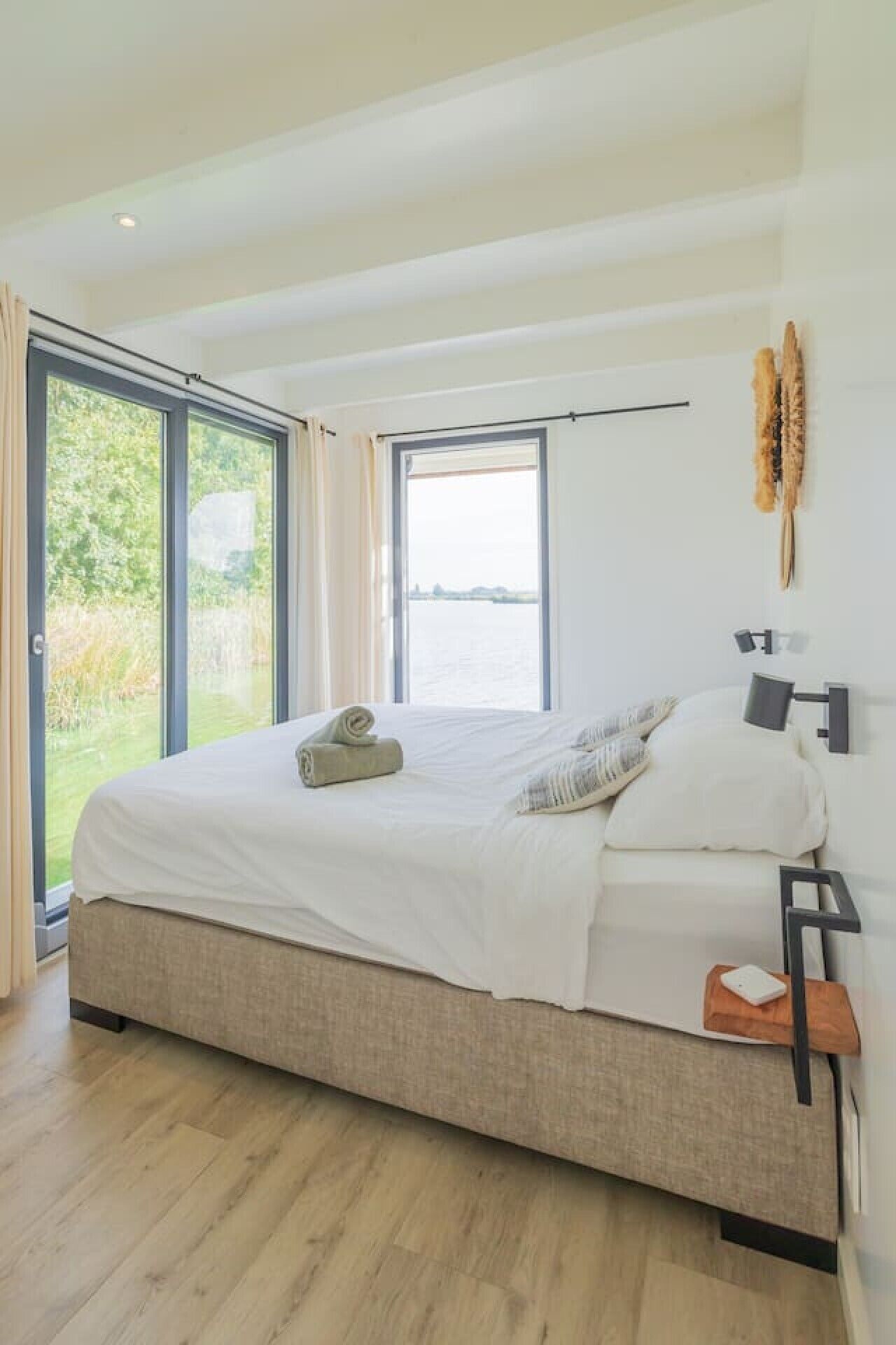 Une chambre moderne avec un grand lit, une vue sur la verdure par les fenêtres et un design minimaliste.