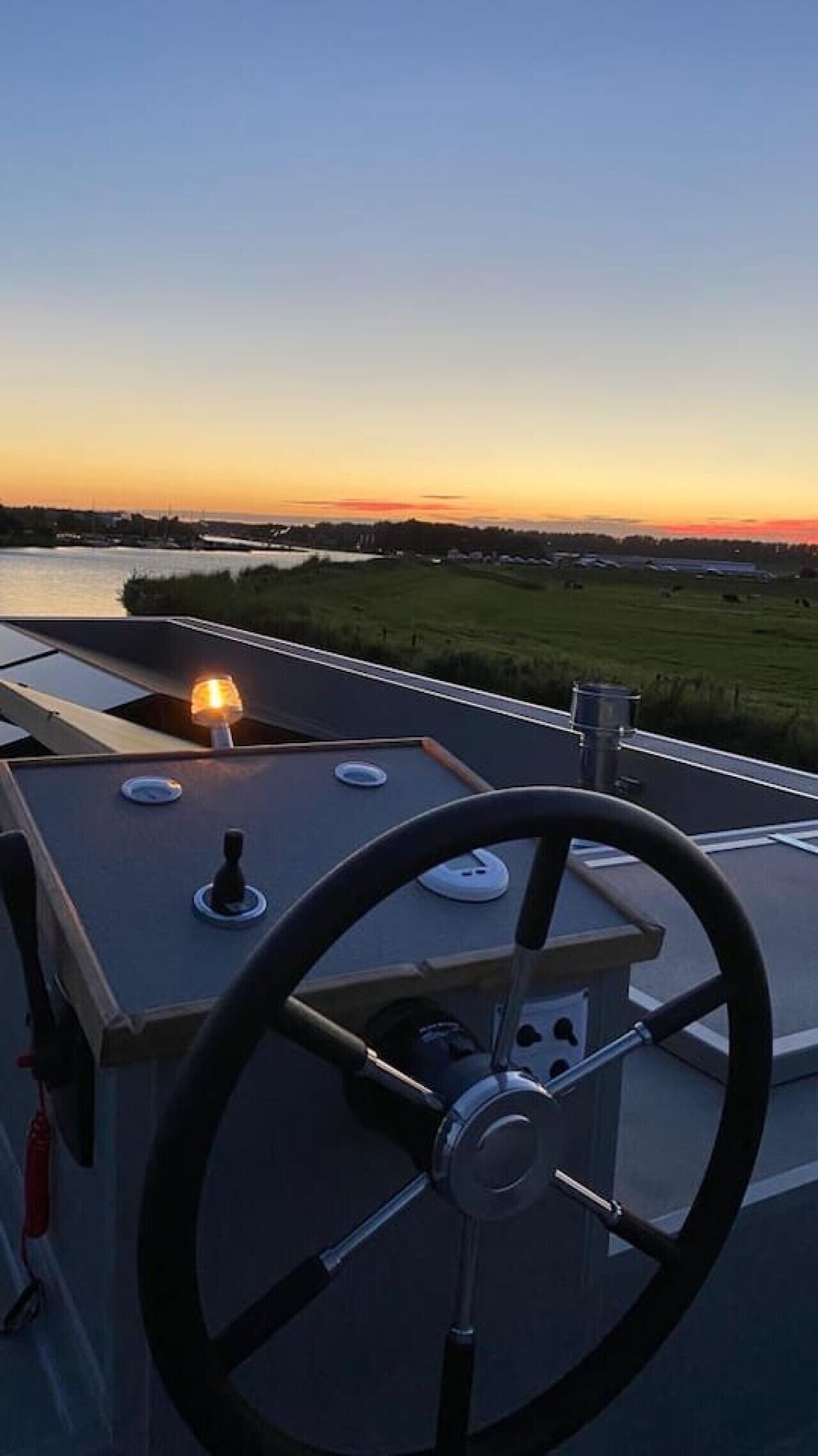Un poste de contrôle équipé d’un volant, d’un tableau de bord et offrant une vue sur un coucher de soleil se reflétant sur une étendue d’eau.