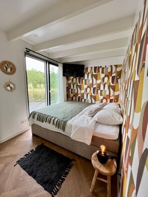 A bedroom with a large bed, a window, a television, and a patterned wall.