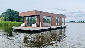 Een modern drijvend huis met grote ramen, een plat dak en een terras met zitplaatsen.