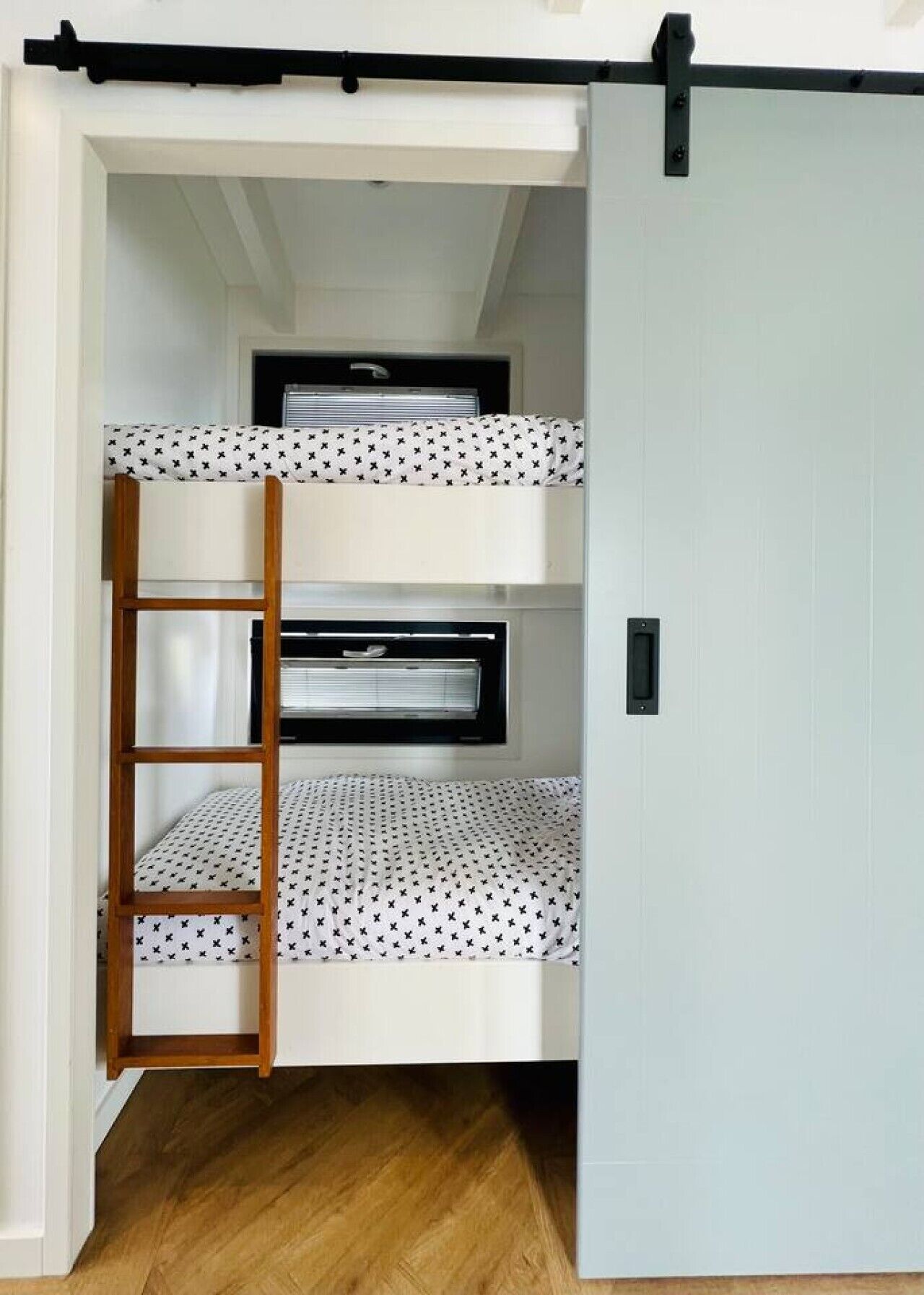 A bunk bed with a ladder, a window with blinds, and a door.
