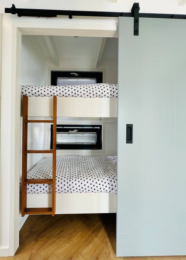 A bunk bed with a ladder, a window with blinds, and a door.