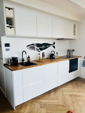 A modern kitchen with white cabinetry, a wooden countertop, a black kettle, and a coffee maker.