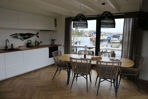 Ett modernt kök med vita skåp, en bänkskiva i trä och en matplats med flätade stolar och ett runt bord.