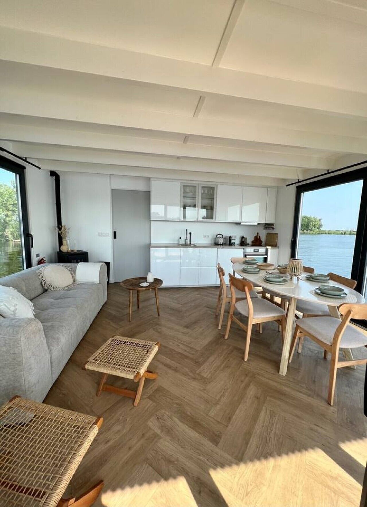 Un intérieur moderne comprenant un coin repas, une cuisine et une grande fenêtre donnant sur un plan d’eau.