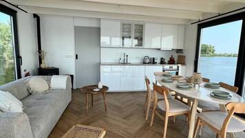 Un intérieur moderne comprenant un coin repas, une cuisine et une grande fenêtre donnant sur un plan d’eau.