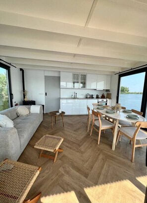 A modern interior with a dining area, kitchen, and a large window overlooking a body of water.