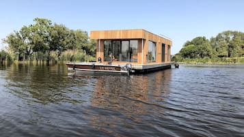 Een rietgedekte drijvende woning met grote ramen en een plat dak, dobberend op kalm water.