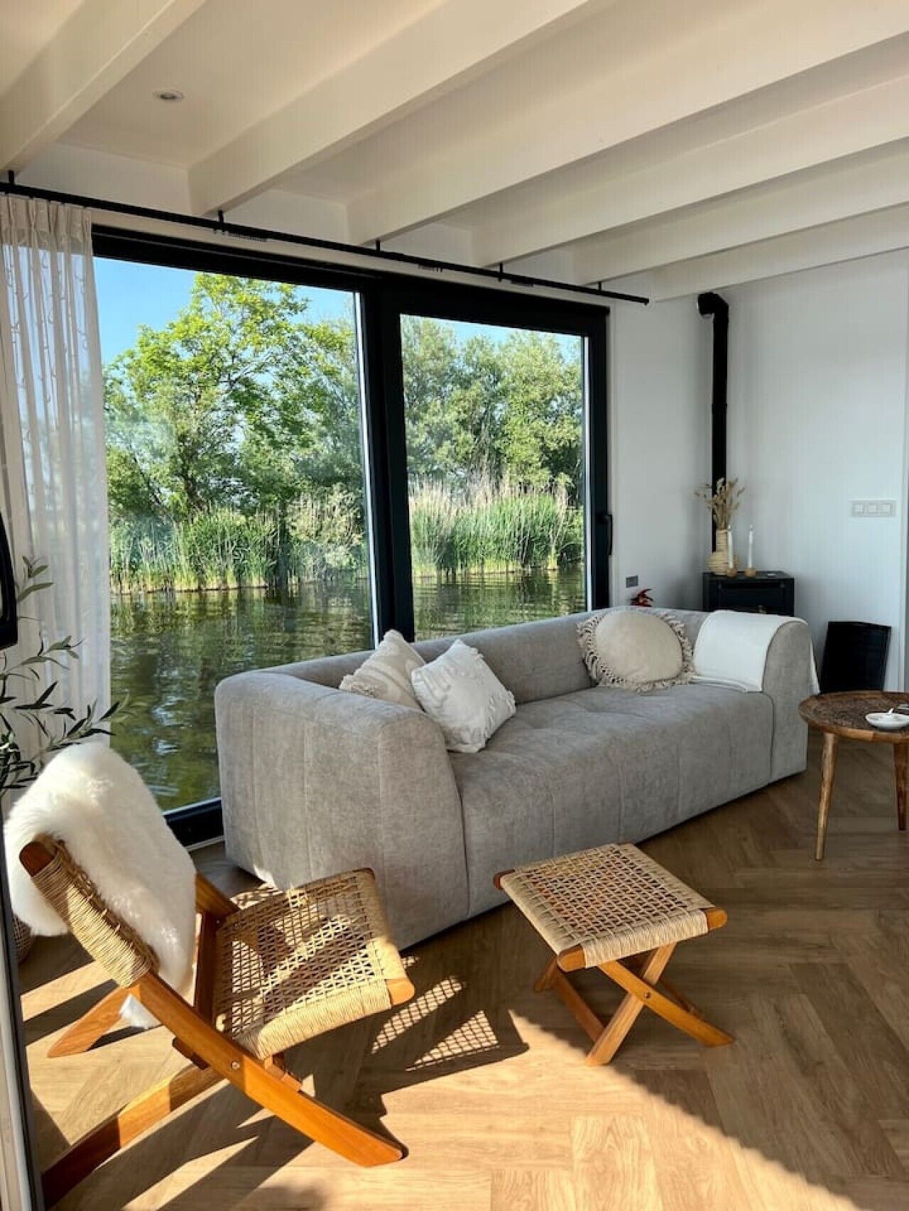 Een moderne woonkamer met een bank, twee schommelstoelen en uitzicht op een waterpartij door grote ramen.