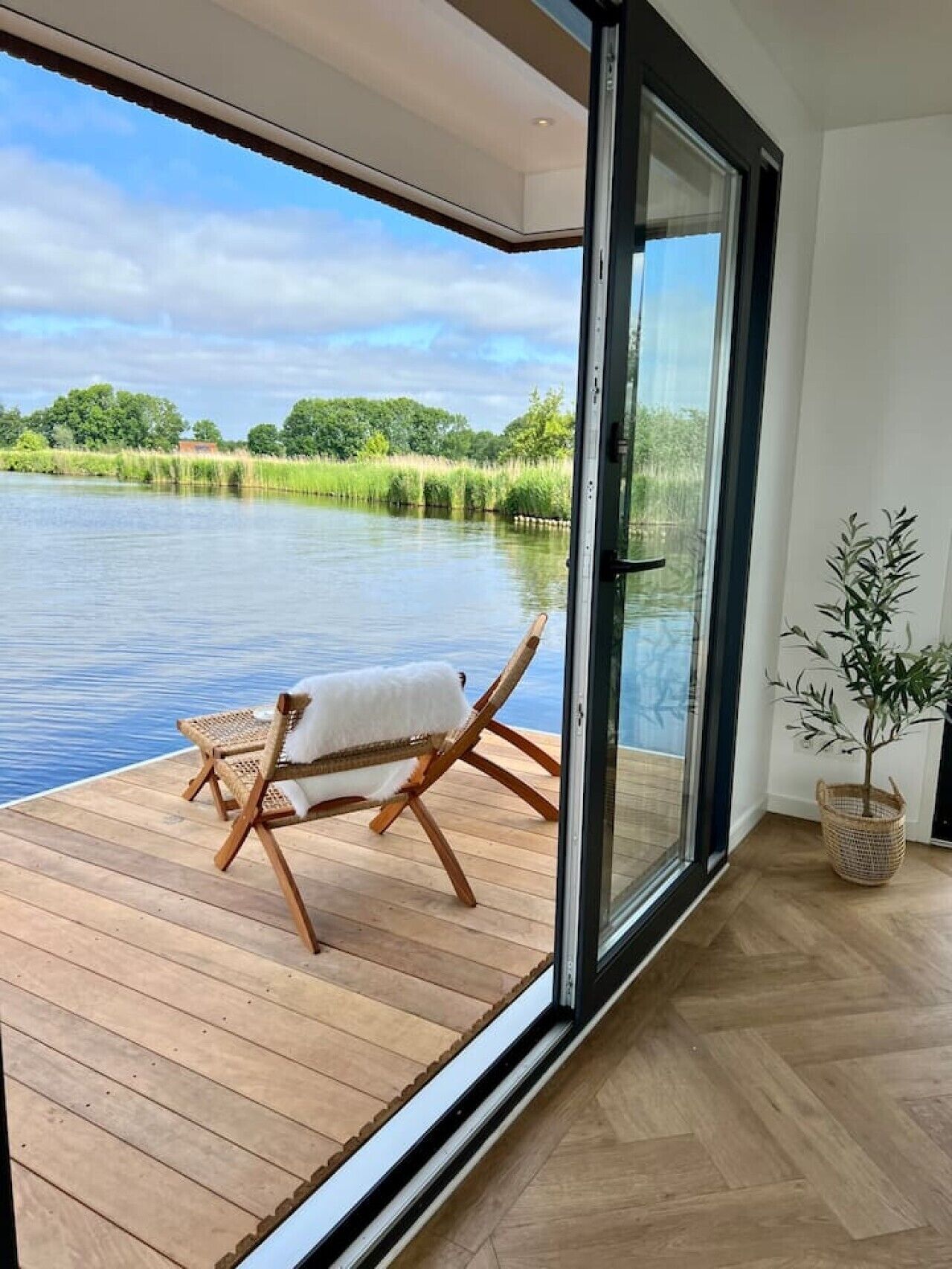 Een kamer met een grote schuifglazen deur die uitkomt op een houten terras met uitzicht op water.
