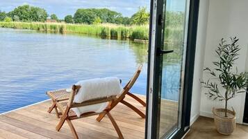 Een kamer met een grote schuifglazen deur die uitkomt op een houten terras met uitzicht op water.