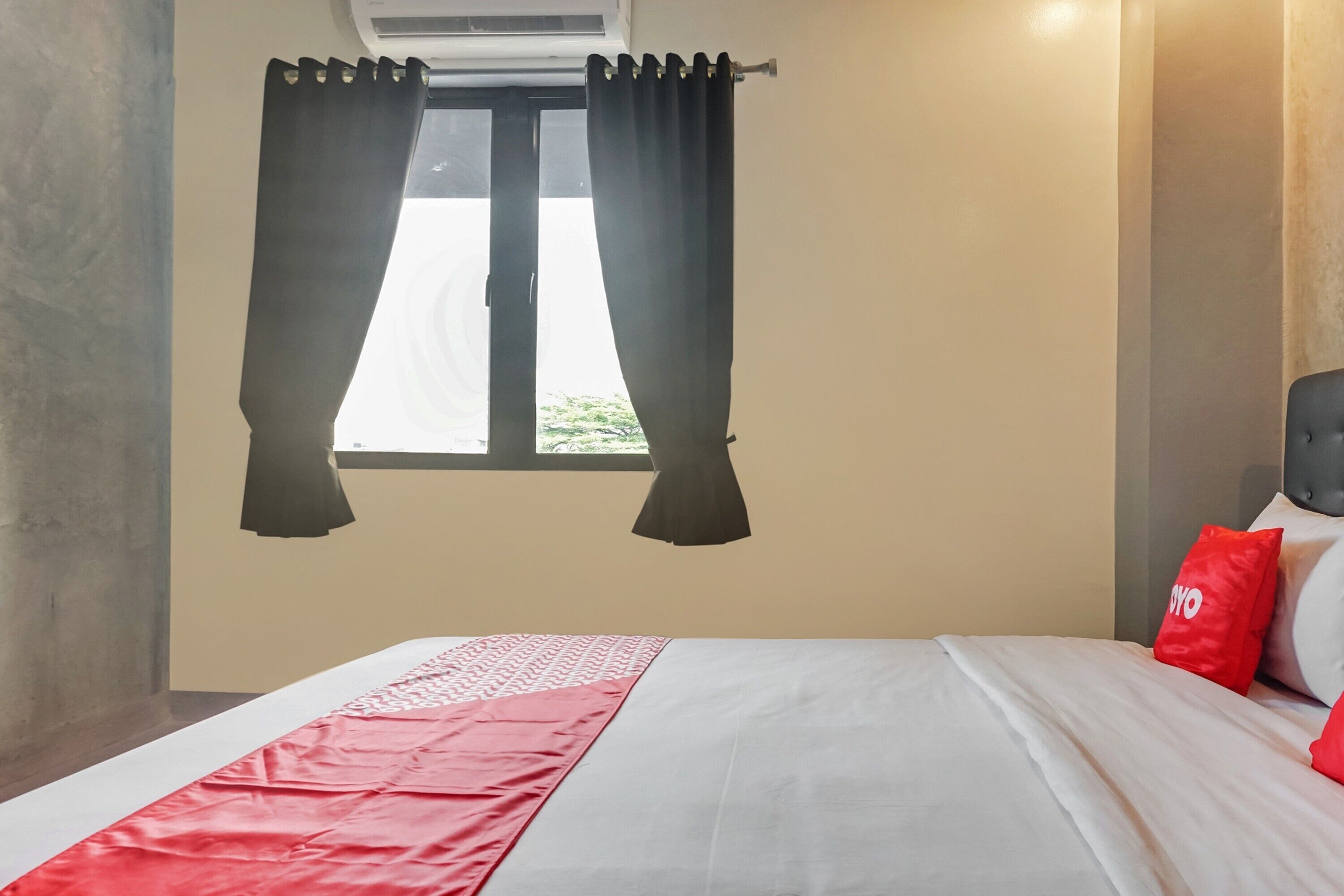 A hotel room with a bed, a window with curtains, and a wall-mounted air conditioner.