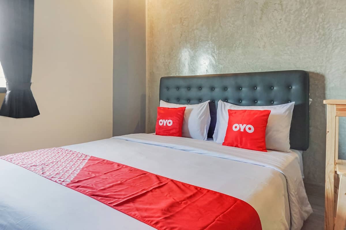 A hotel room with a bed featuring a red and white bedspread and two pillows with the word "OYO" on them.