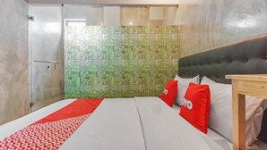 Ein Hotelzimmer mit Bett, Nachttisch aus Holz, Duschkabine aus Glas und einer Wand mit Muster.