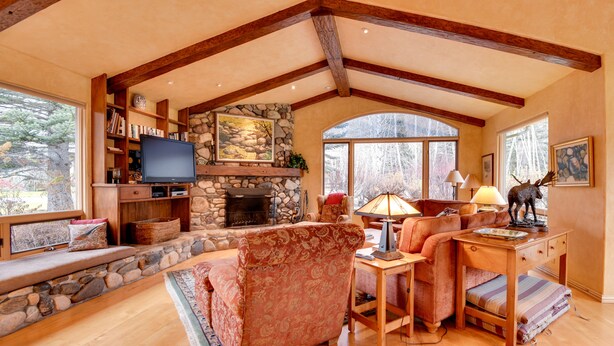 A cozy living room with a stone fireplace, wooden beams, and a large window offering a view of trees. - 2 Mi to River Run Day Lodge: Family-Friendly Home (Sun Valley)