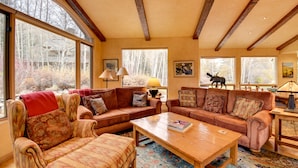 A cozy living room with two sofas, a coffee table, and large windows offering a view of trees and a statue. - 2 Mi to River Run Day Lodge: Family-Friendly Home (Sun Valley)