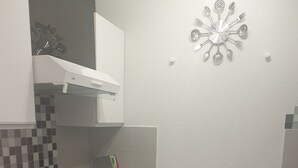 Cocina compacta con microondas, refrigerador pequeño, lavamanos y un basurero.