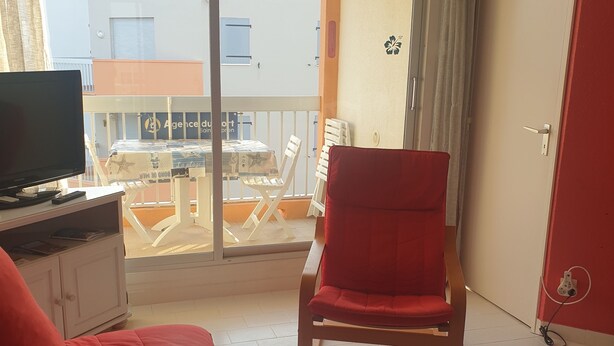 Una habitación de hotel con una cama, una silla roja, una mesita pequeña y un televisor sobre un mueble.