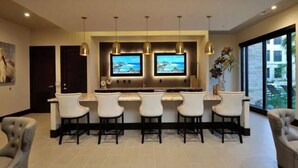 Una cocina moderna con barra, dos televisores, luces colgantes y un ventanal grande.