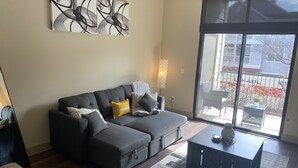 Una sala de estar moderna con un sofá seccional gris, una pequeña mesa de centro negra y un gran ventanal con vistas a la calle.