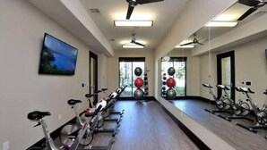 Un gimnasio con bicicletas estáticas, pelotas de ejercicio y un amplio muro con espejos.