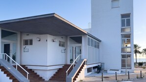 A modern building with a flat roof, a staircase leading to a covered entrance, and a small balcony with a scooter parked nearby.