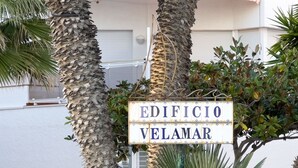A sign with 'EDIFICIO VELAMAR' written on it, surrounded by palm trees and a building in the background.