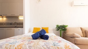 A bedroom with a bed, a sofa, a potted plant, and a kitchenette.